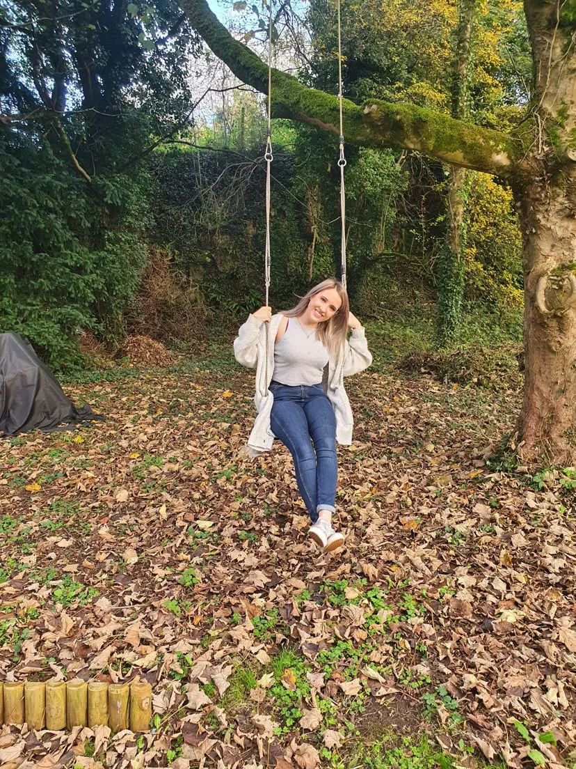 Alice McCorry sitting on a garden swing among autumn leaves